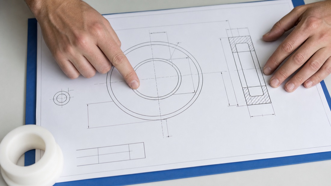 Manos señalando un plano técnico de una pieza circular de PTFE junto a una muestra blanca.